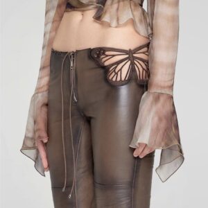 Detalle de pantalones de efecto cuero en tono marrón con diseño lateral en forma en mariposa bordada, estilo cut-out.
